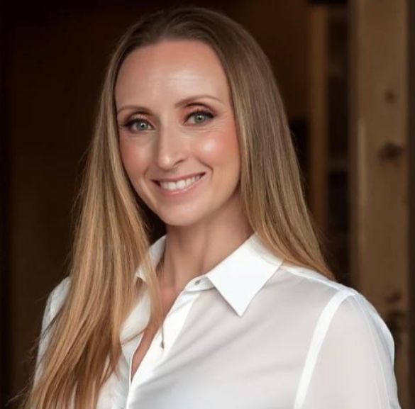 A woman with long blonde hair is wearing a white shirt and smiling.