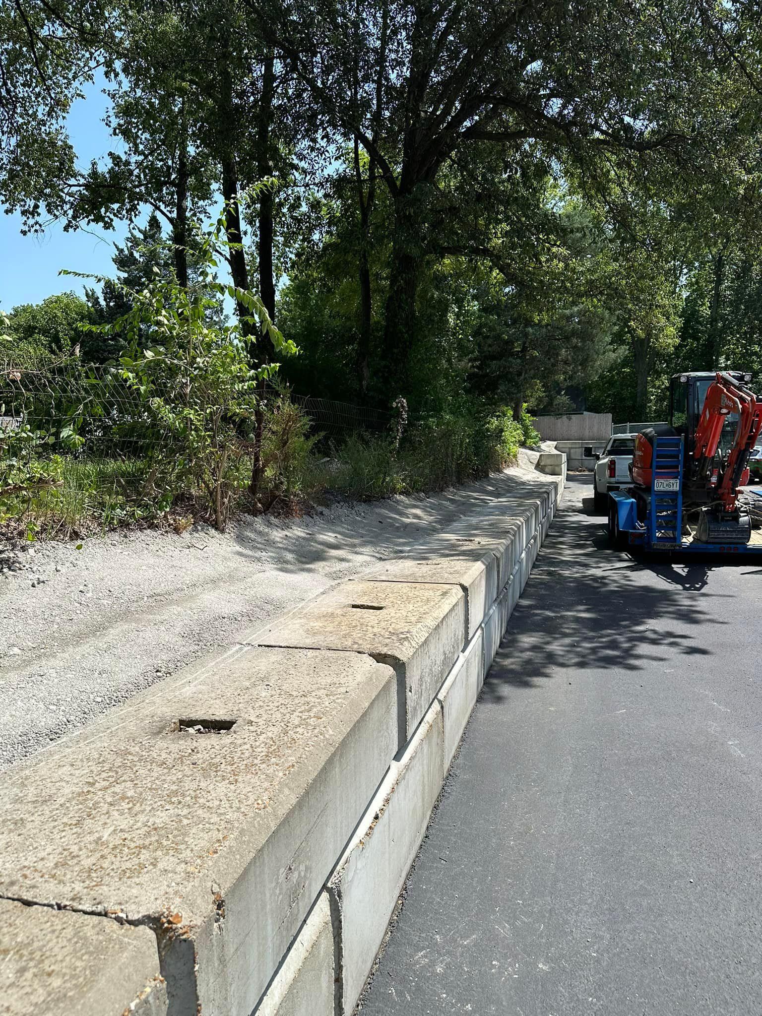 A construction vehicle is parked on the side of the road next to a concrete wall.