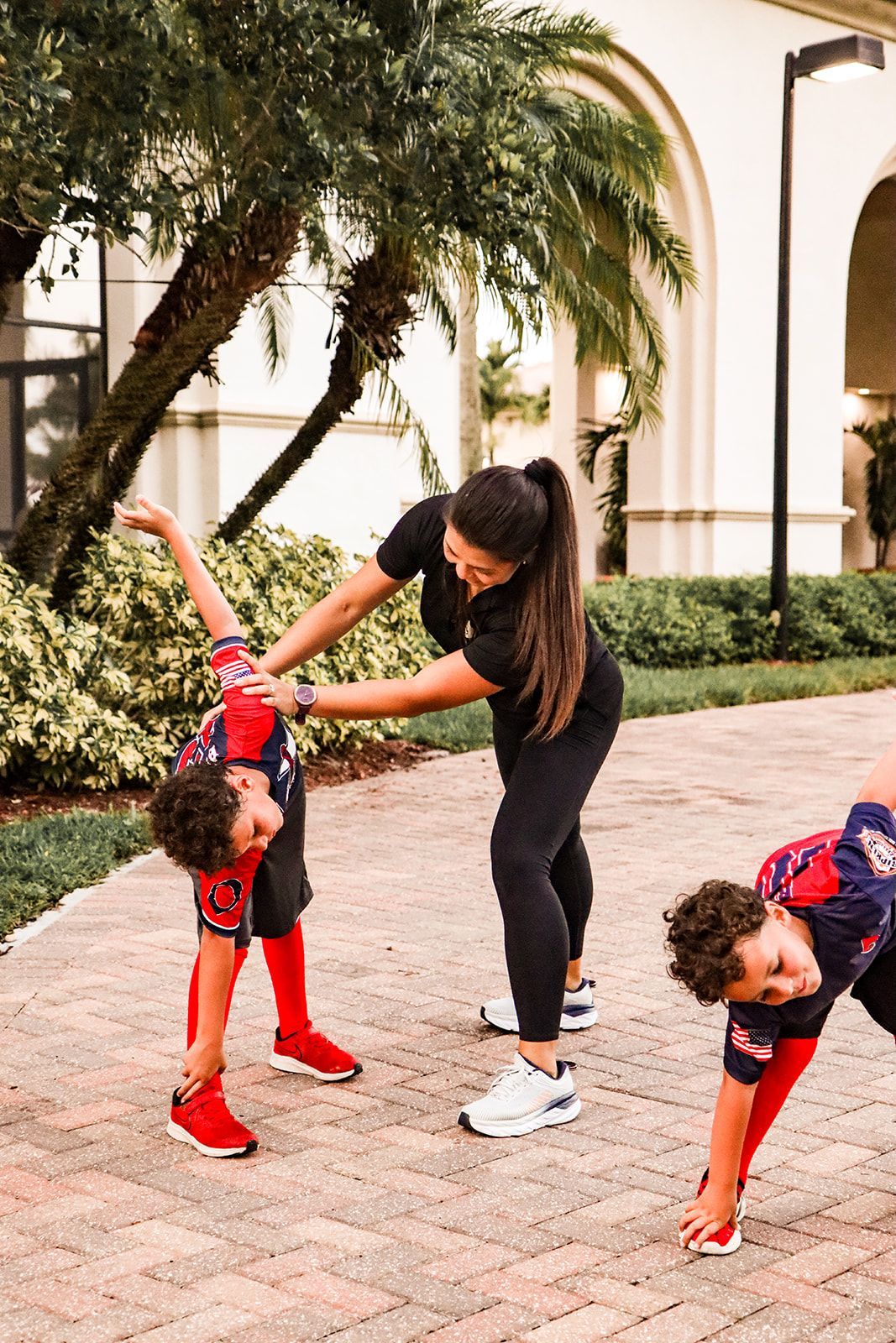 A woman and two children are doing stretching exercises on a sidewalk.