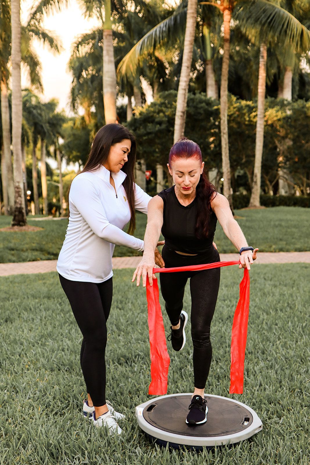 A woman is helping another woman do exercises with a resistance band.