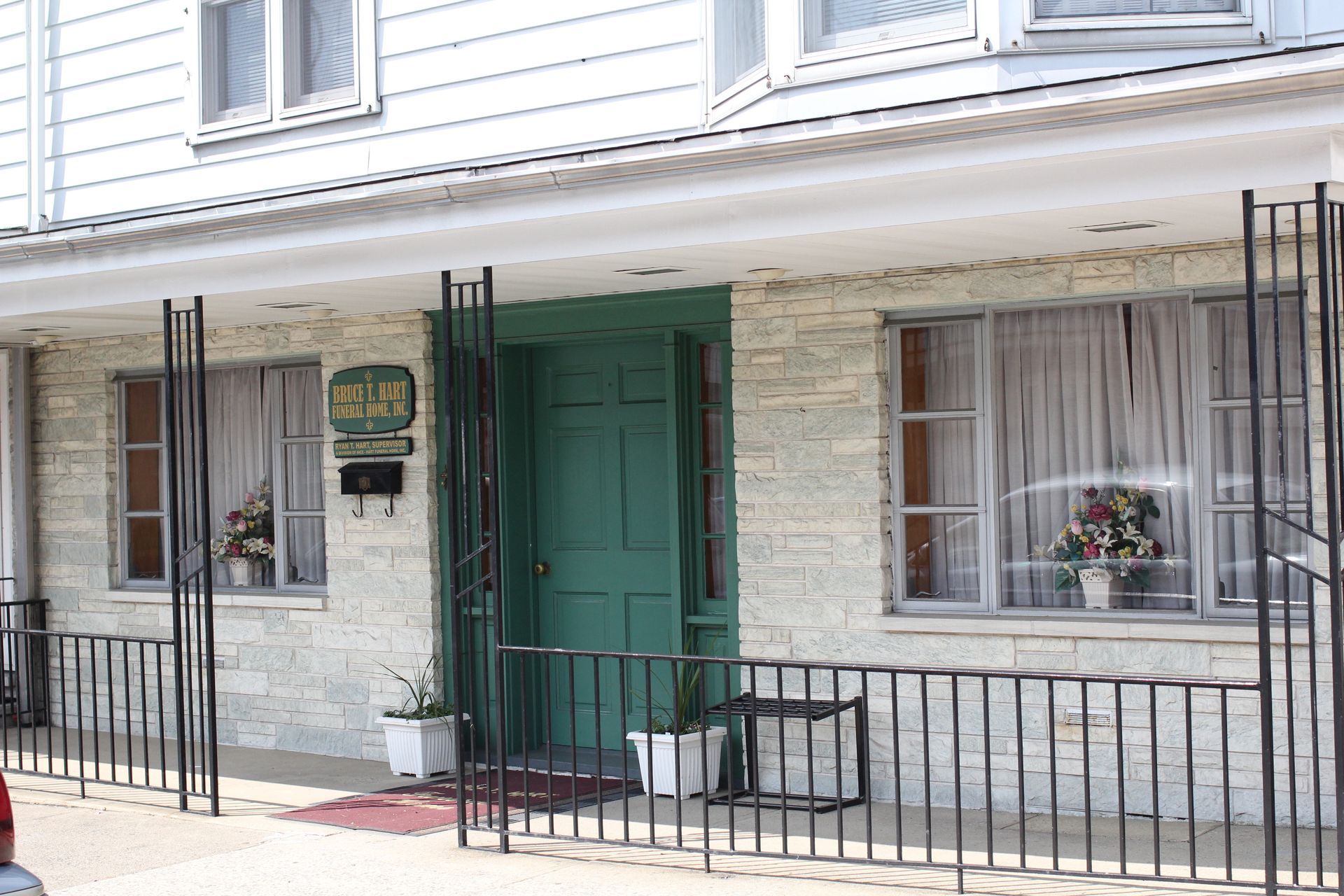 A white brick building with a green door and a black fence