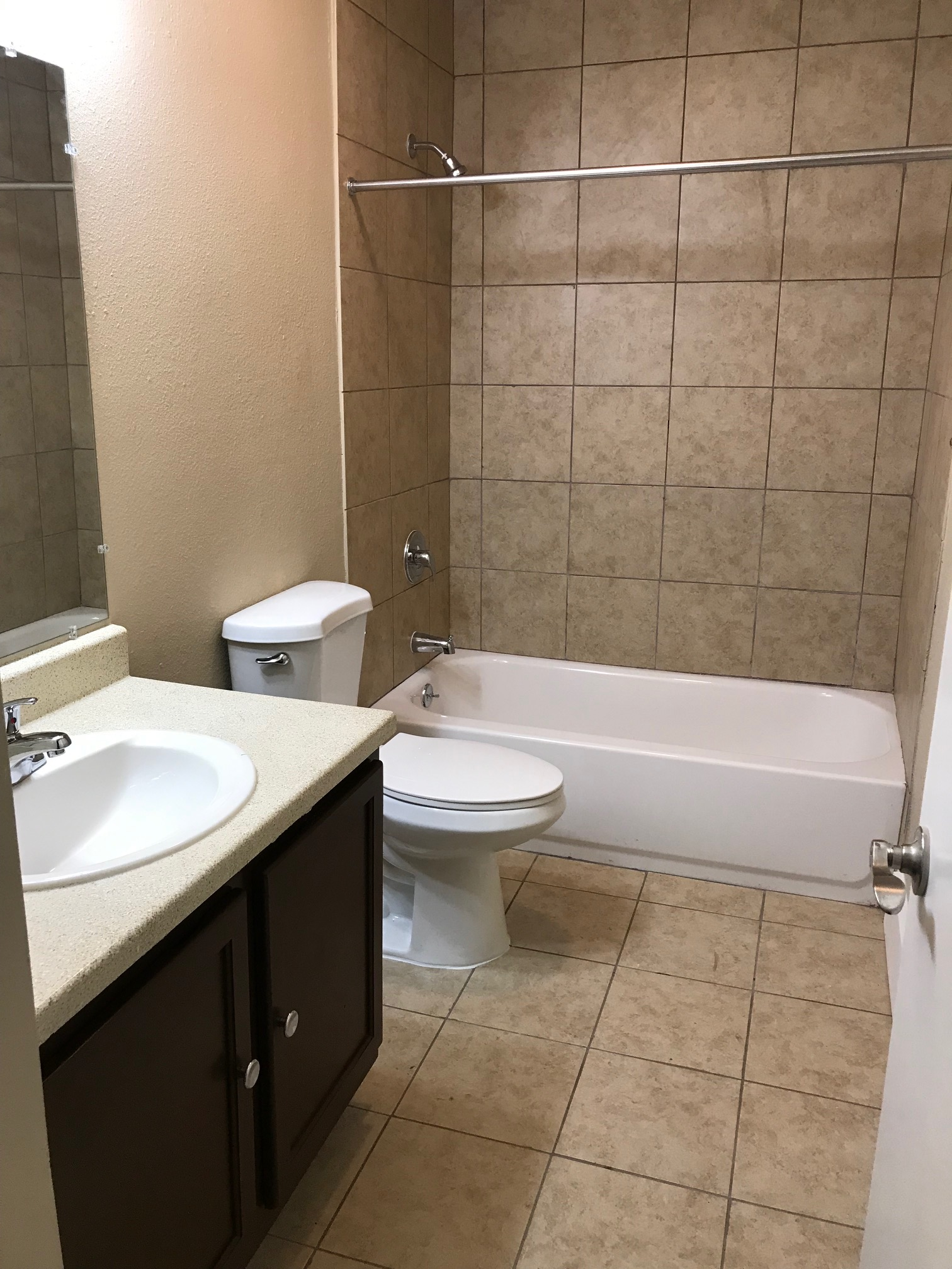 Bathroom with brown vanity, white sink and toilet, beige tile walls, and a white bathtub.