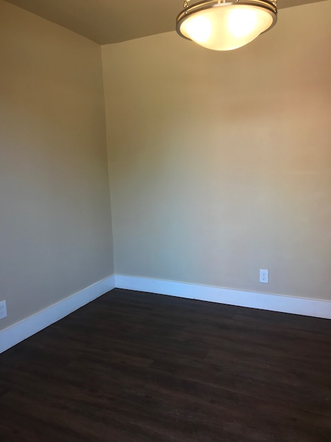 Empty room with brown flooring, beige walls, white trim, and a ceiling light.