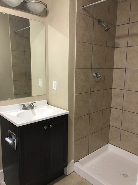 Bathroom with a vanity, mirror, and shower with tan tiles.