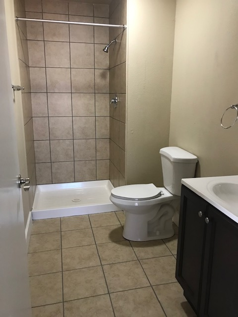Bathroom with beige tile floor, brown shower tile, white toilet and sink, and dark brown cabinet.