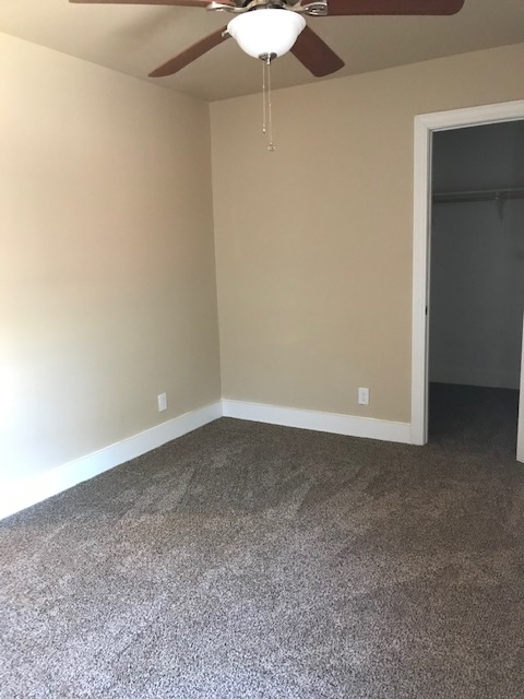 Empty bedroom with tan walls, beige carpet, and open closet door. Ceiling fan visible.