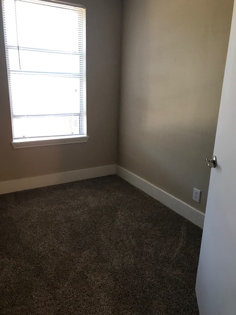 Empty room with brown carpet, beige walls, a window with blinds, and a white door.