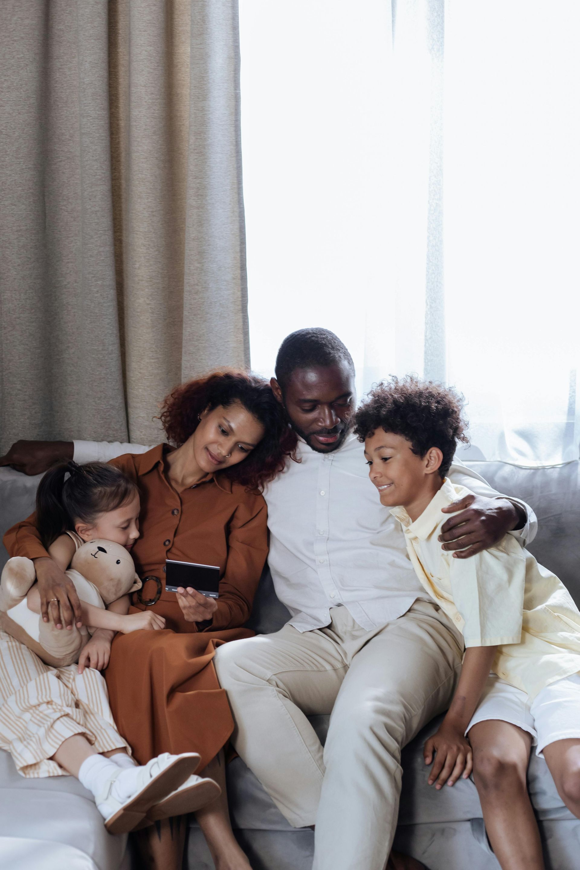 A family is sitting on a couch looking at a cell phone.