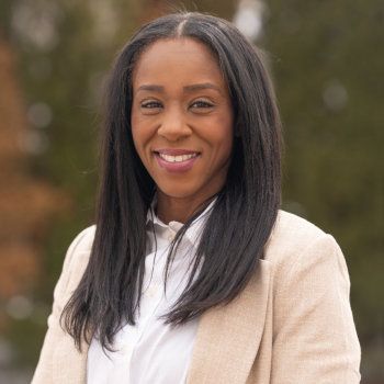 A woman in a tan jacket and white shirt is smiling for the camera.