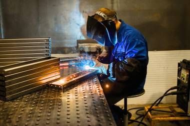 A Man Wearing A Welding Helmet Is Grinding A Piece Of Metal In A Factory — Real Engineering In West Gosford, NSW