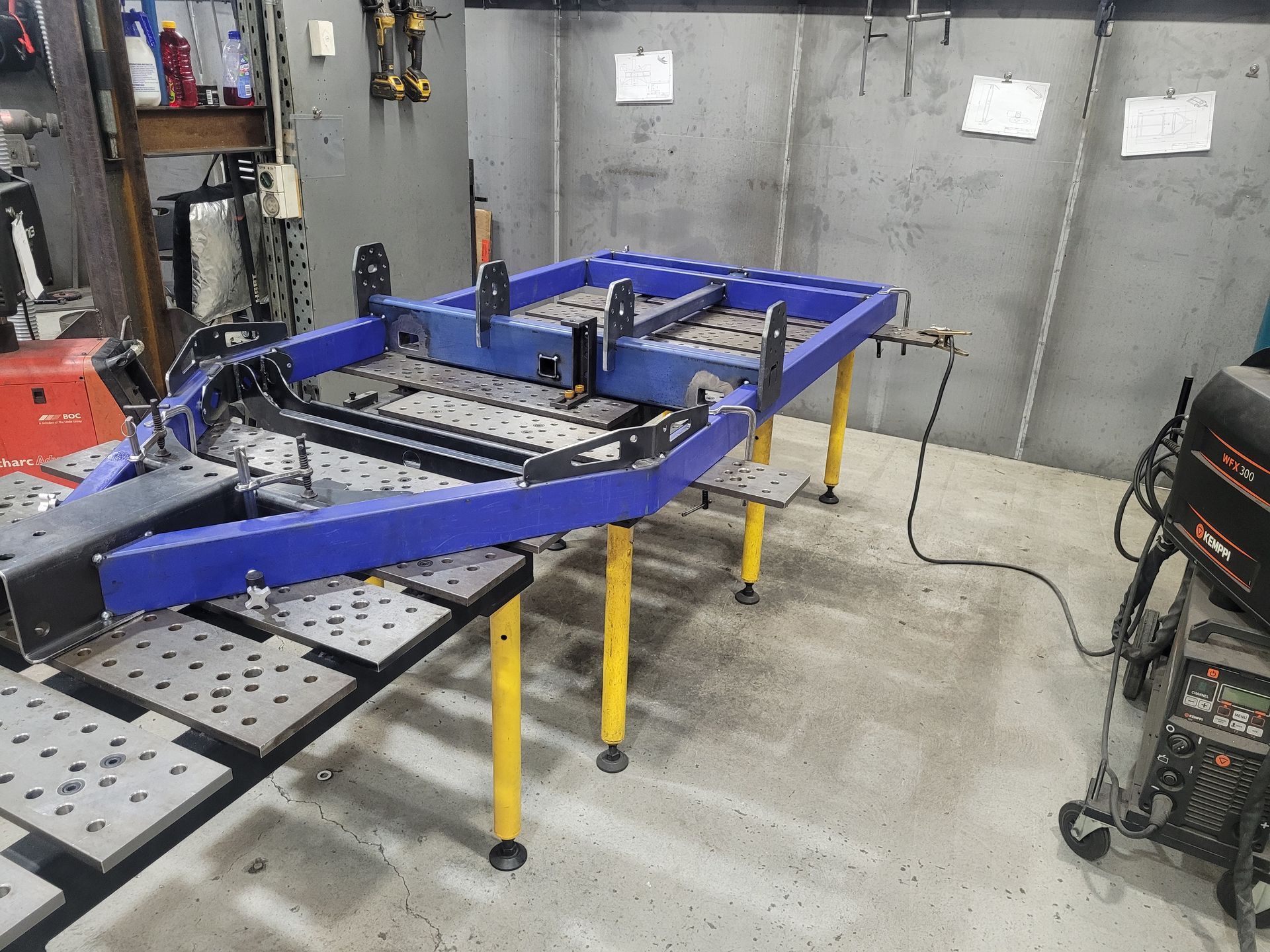 Blue metal vehicle frame on yellow stands in a workshop, with tools and equipment nearby. — Real Engineering in Ingleburn, NSW