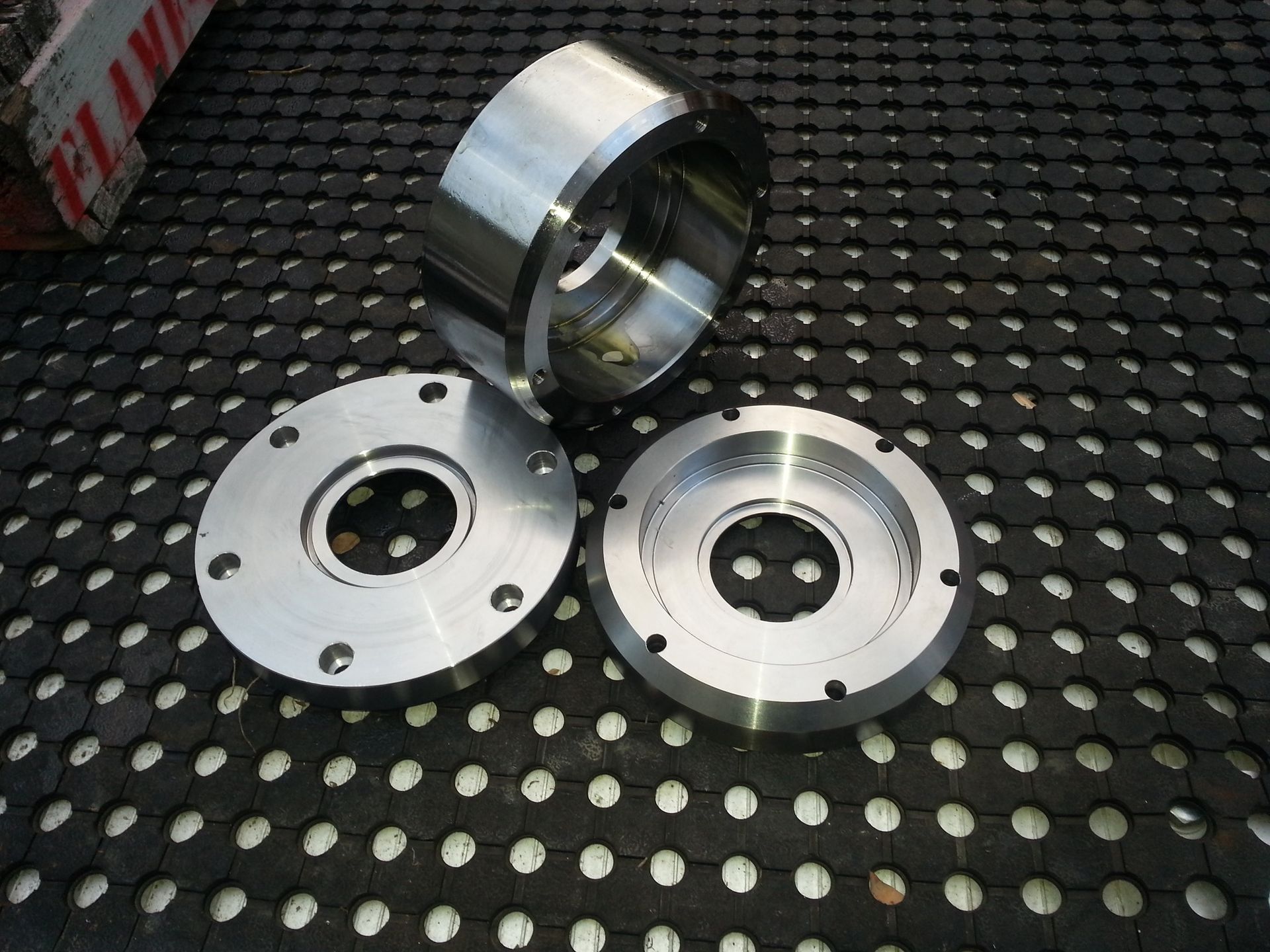 Three Metal Machine Parts On A Black Perforated Surface — Real Engineering in West Gosford, NSW