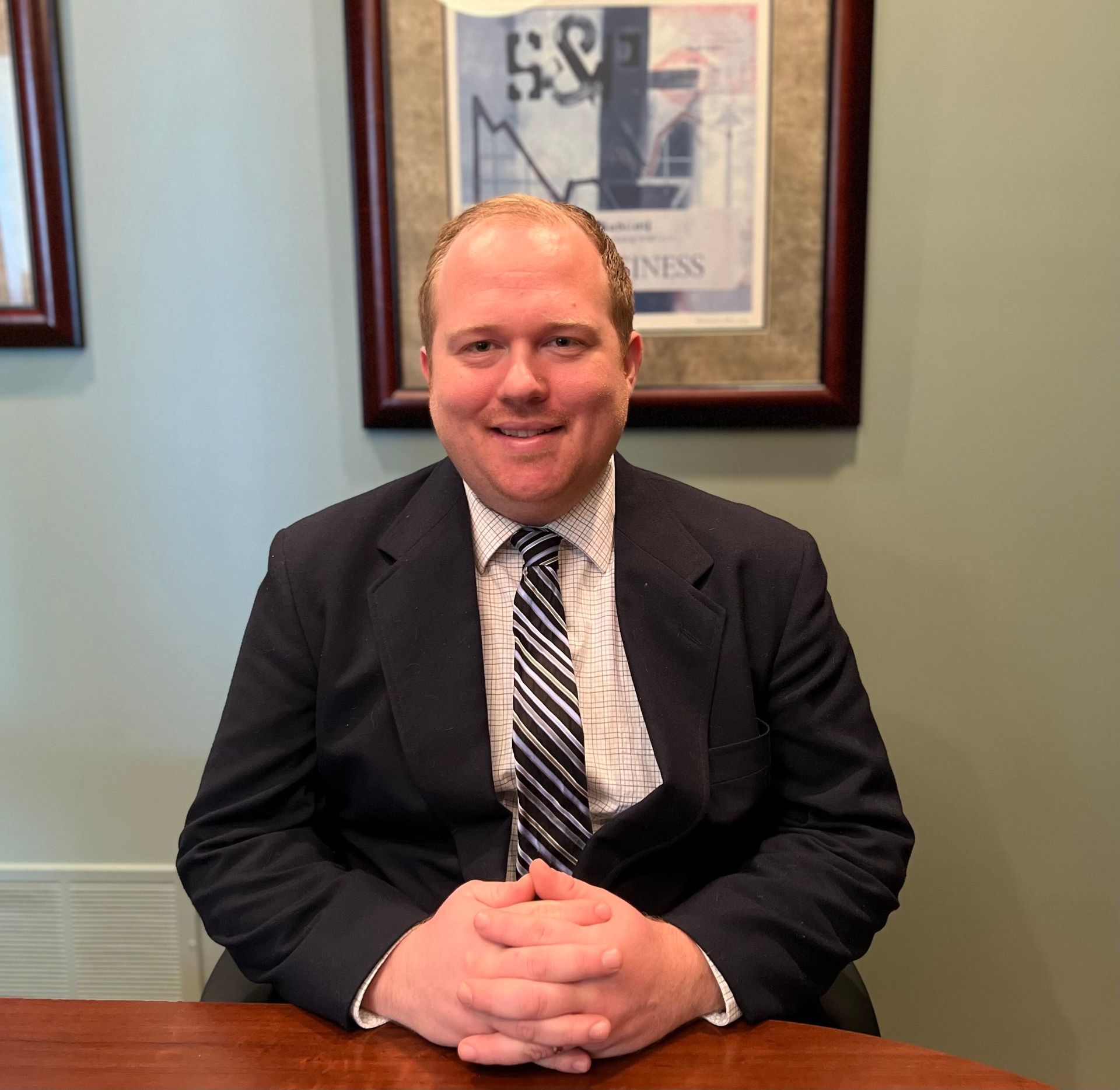 A man in a suit and tie is sitting at a table with his hands folded