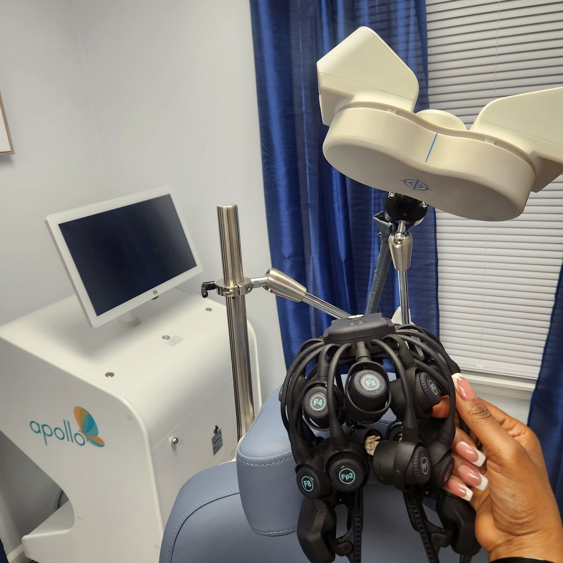 Person holding a black head device used in a medical setting, with white machine in background.