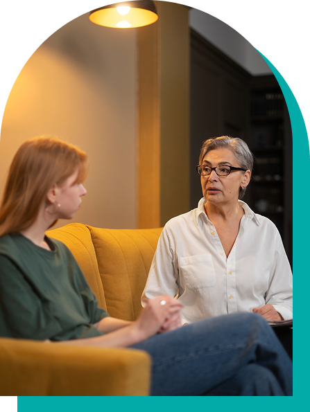 Woman in therapy session on yellow couch, talking to a client.