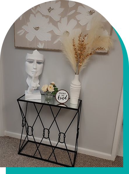 A decorative black metal side table with a white bust sculpture, vase, and flowers. Neutral-toned wall art.