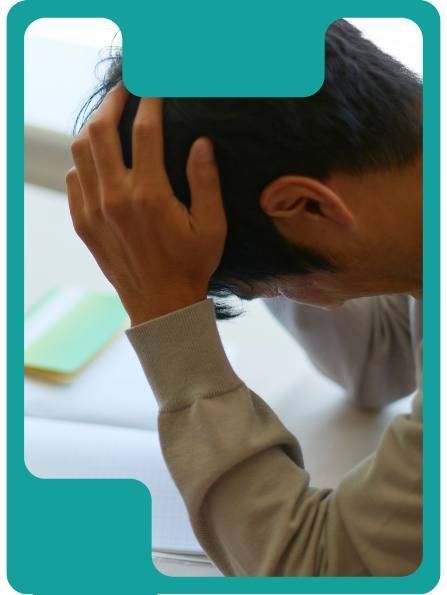 Person with head in hands, appears stressed. Gray sweater, white surface, light blue border.