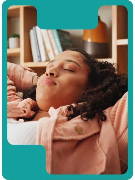Woman relaxing with eyes closed, leaning back, in front of a bookshelf. Pink shirt.