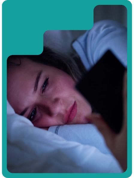 Woman in bed looking at a phone screen. Face illuminated by phone light, possibly at night.