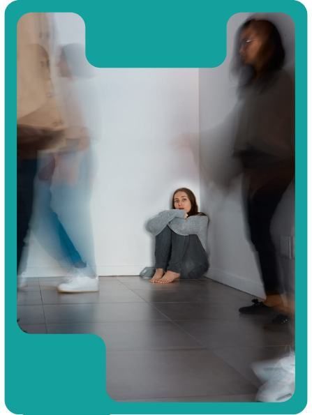 Woman huddled in a corner, surrounded by blurred figures.