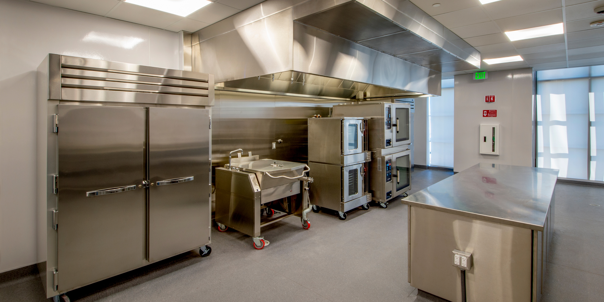 Commercial kitchen with stainless steel appliances, including refrigerators, ovens, and a prep table.