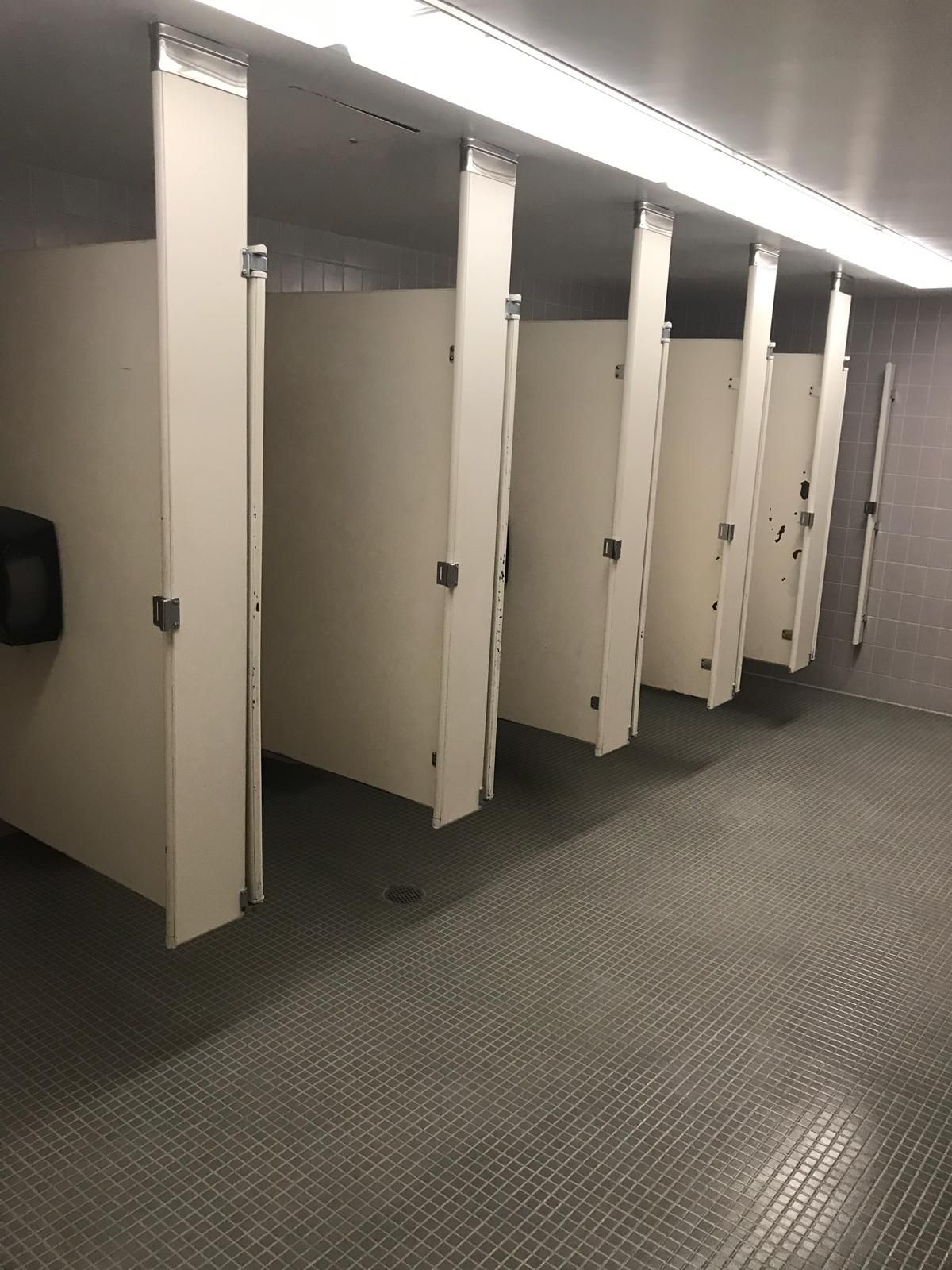Public restroom with six stalls, white doors, and gray speckled floor.