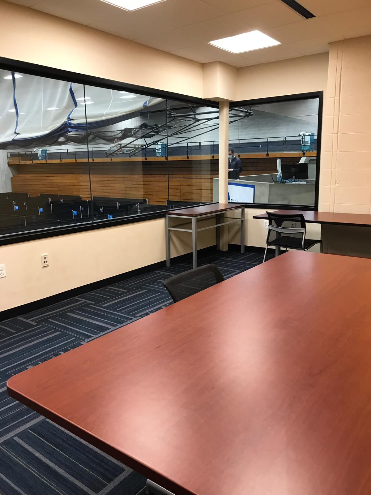 A room with a long table, window overlooking a space, and a small table with a computer.