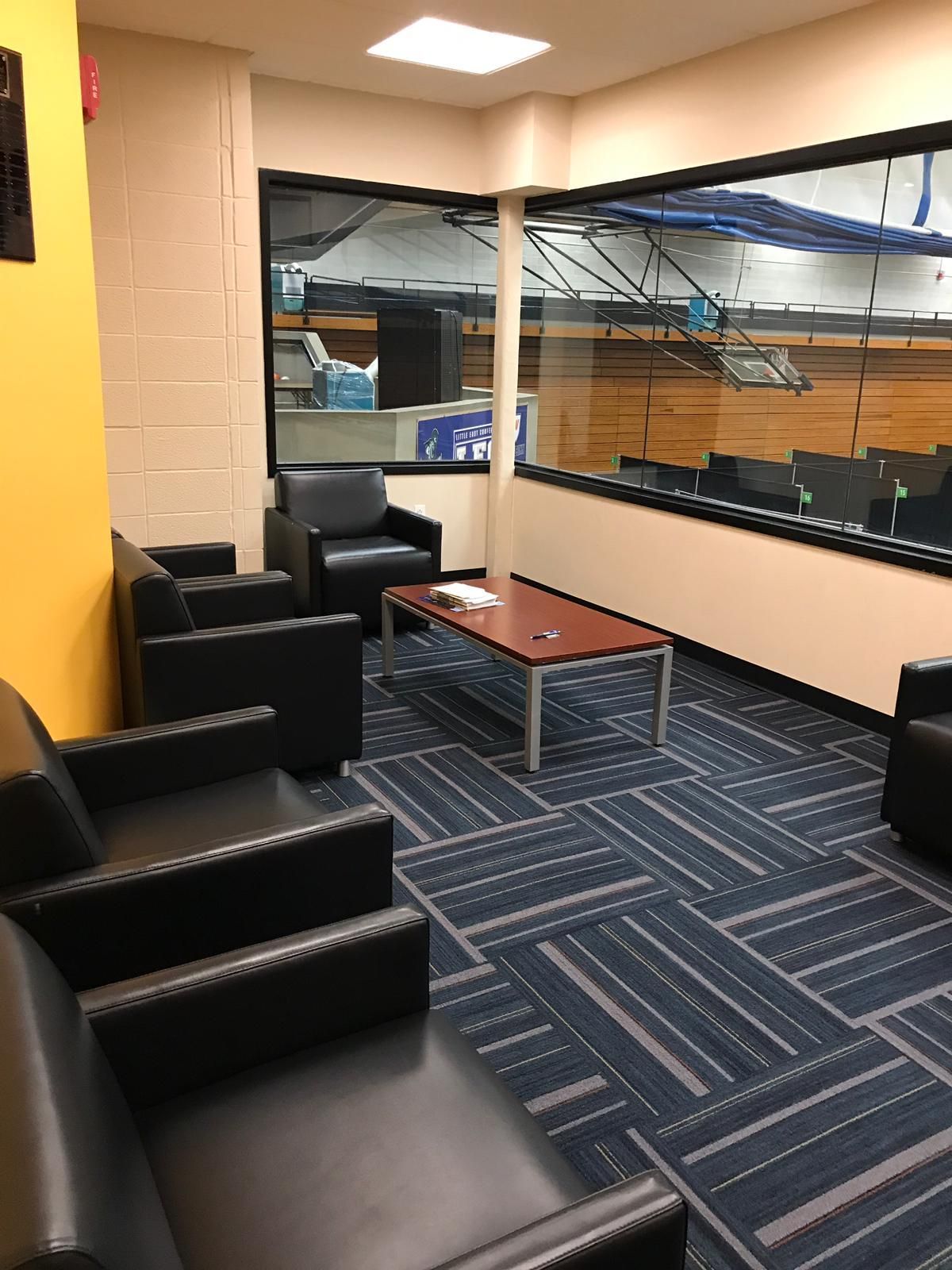 Seating area with black chairs, blue patterned carpet, and a view of a gymnasium.