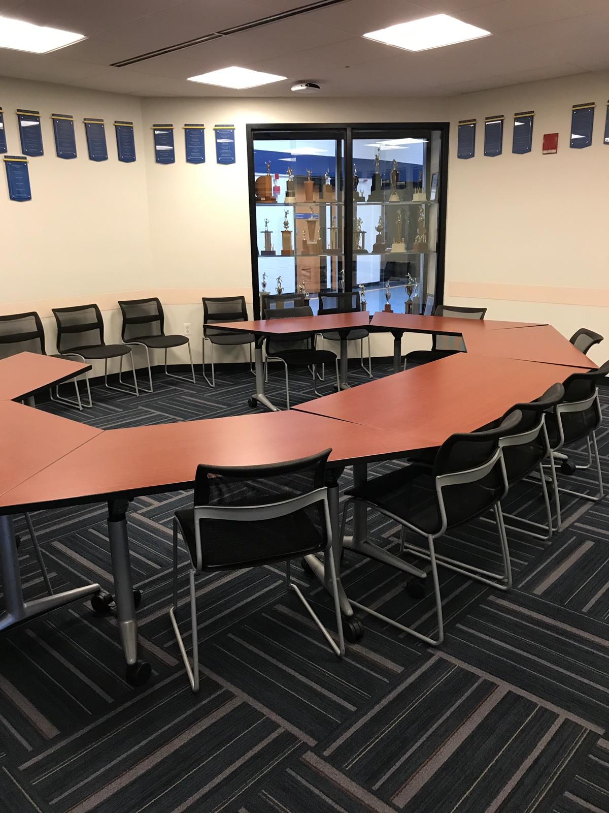 Conference room with a horseshoe-shaped table, black chairs, glass display case, and wall decorations.