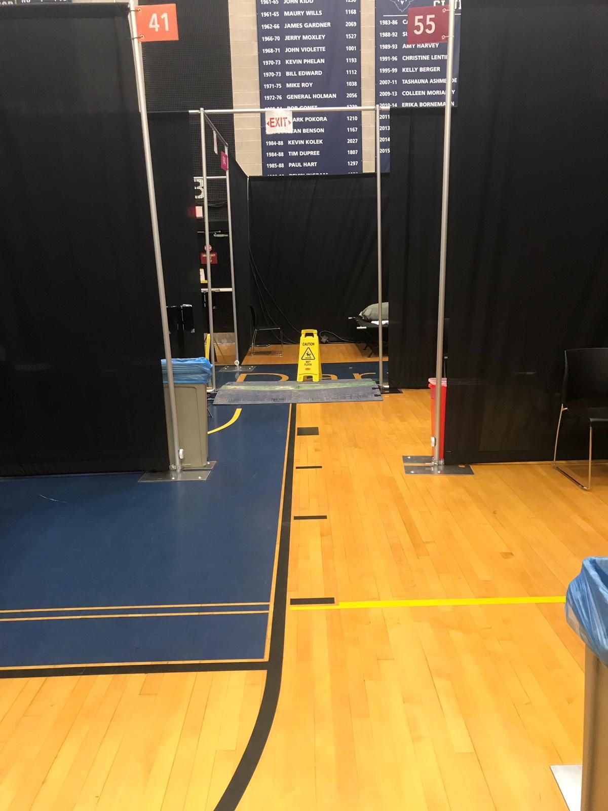 A temporary hallway with black curtains, metal supports, and wet floor sign set up in a gym.