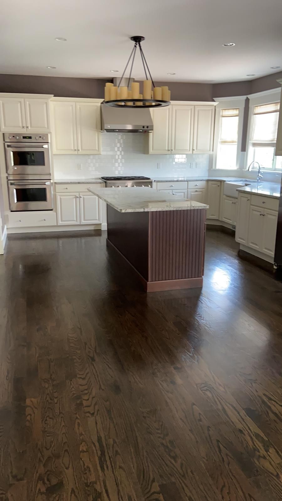 Spacious kitchen with dark wood floors, white cabinets, and a brown island. Stainless steel appliances and a chandelier.