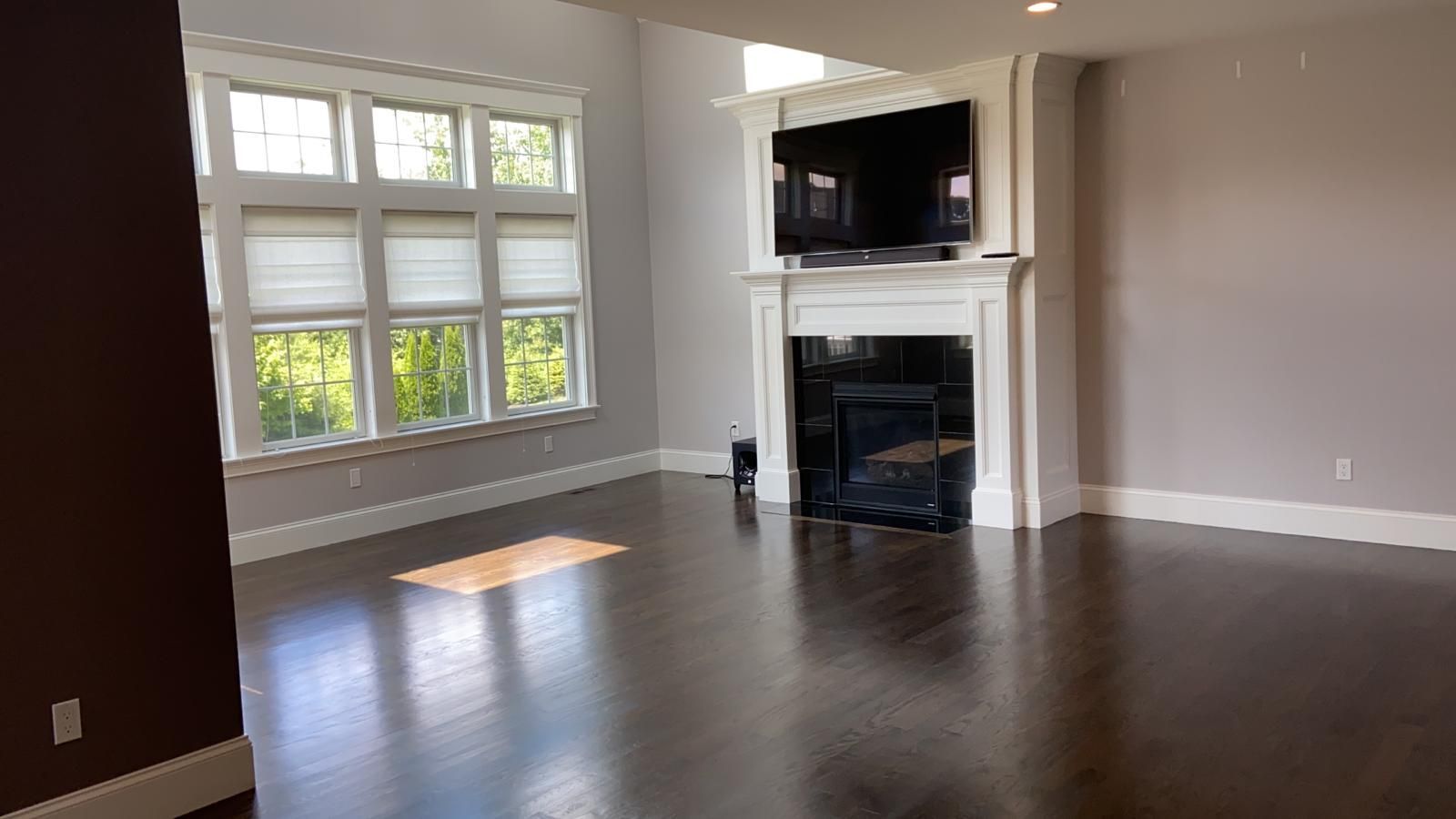 Empty living room with dark wood floor, large window, fireplace, and mounted TV.