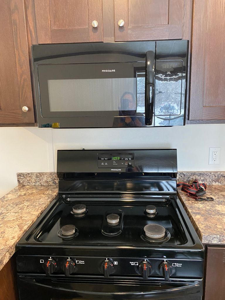Black microwave above a black stove. Brown cabinets and tan countertop.