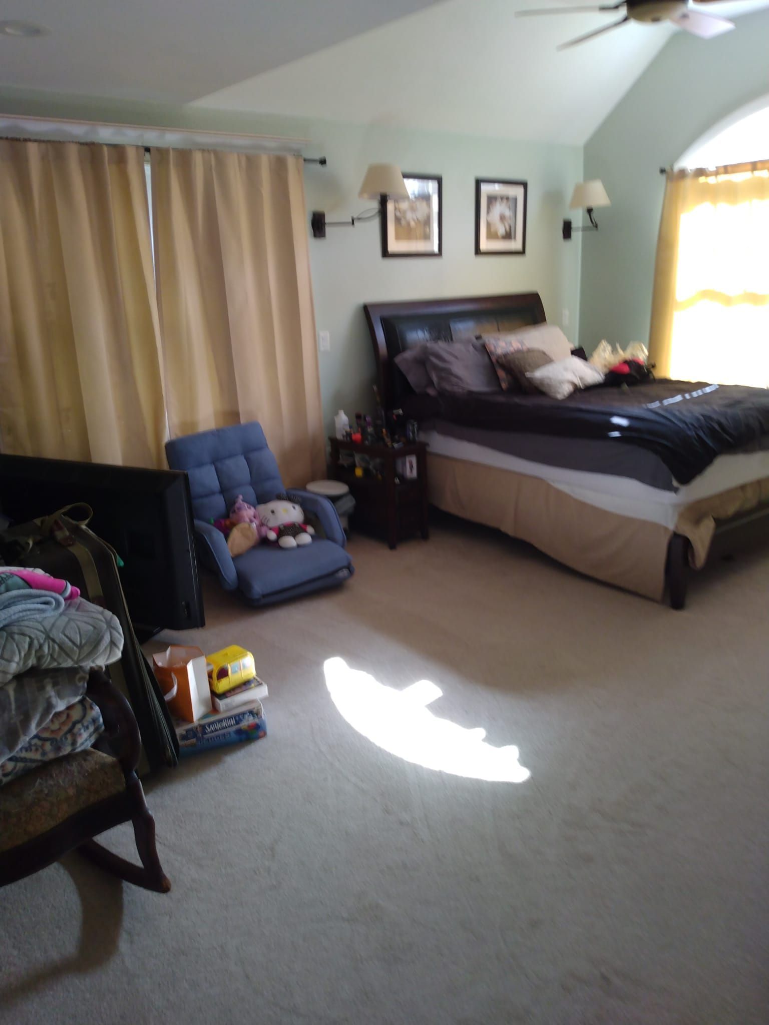 Bedroom with bed, chair, curtains, and sunlight on the carpet.