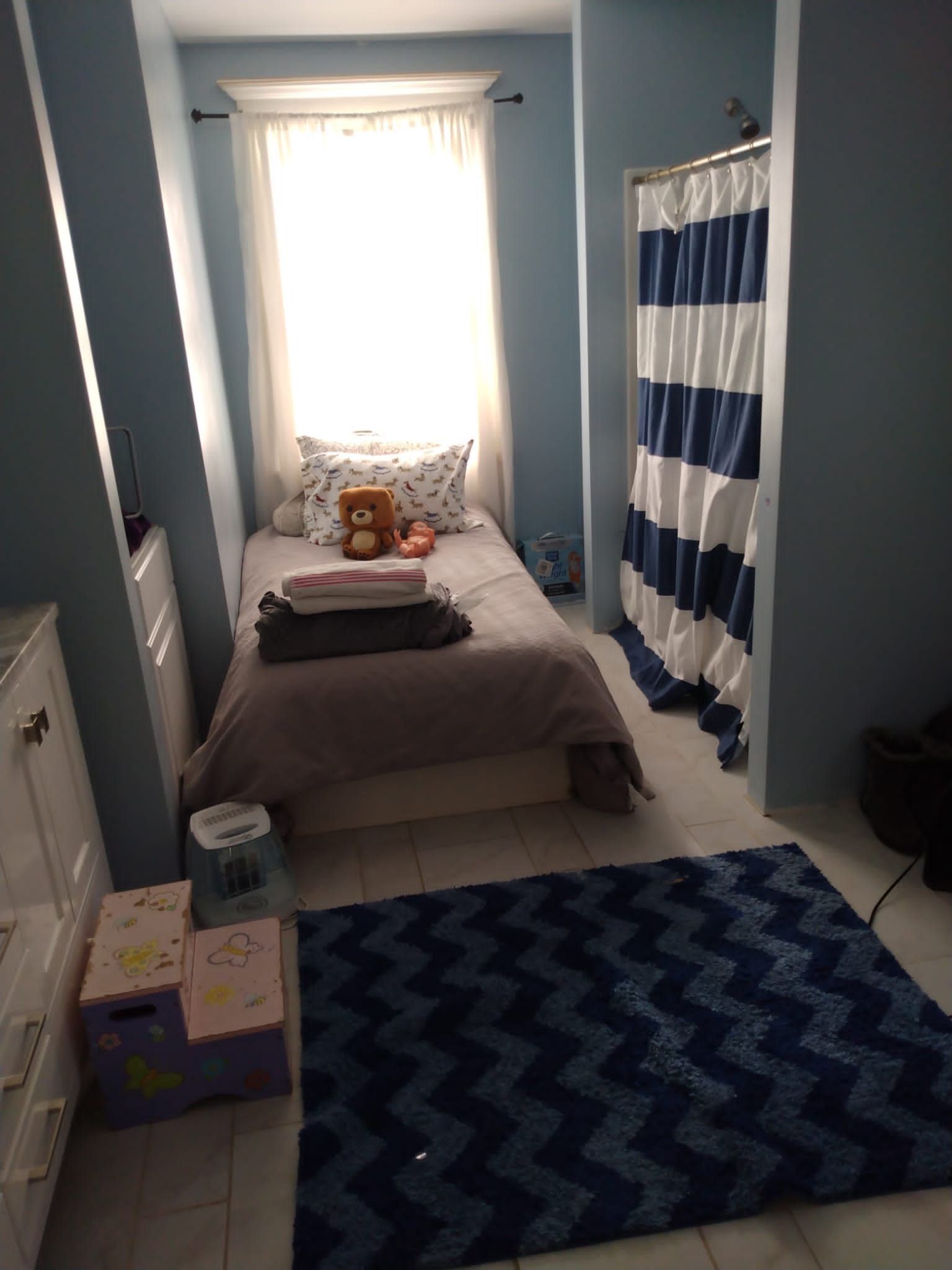 Small bedroom with bed, bathroom, and blue chevron rug.