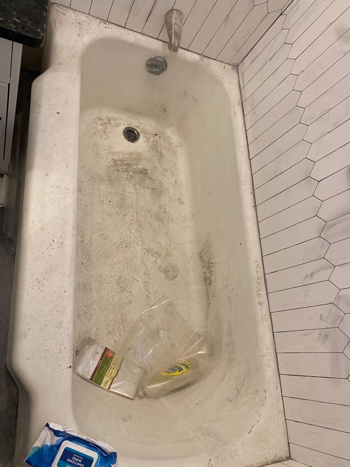 Dirty white bathtub with stains and debris; wet wipes visible on the floor.
