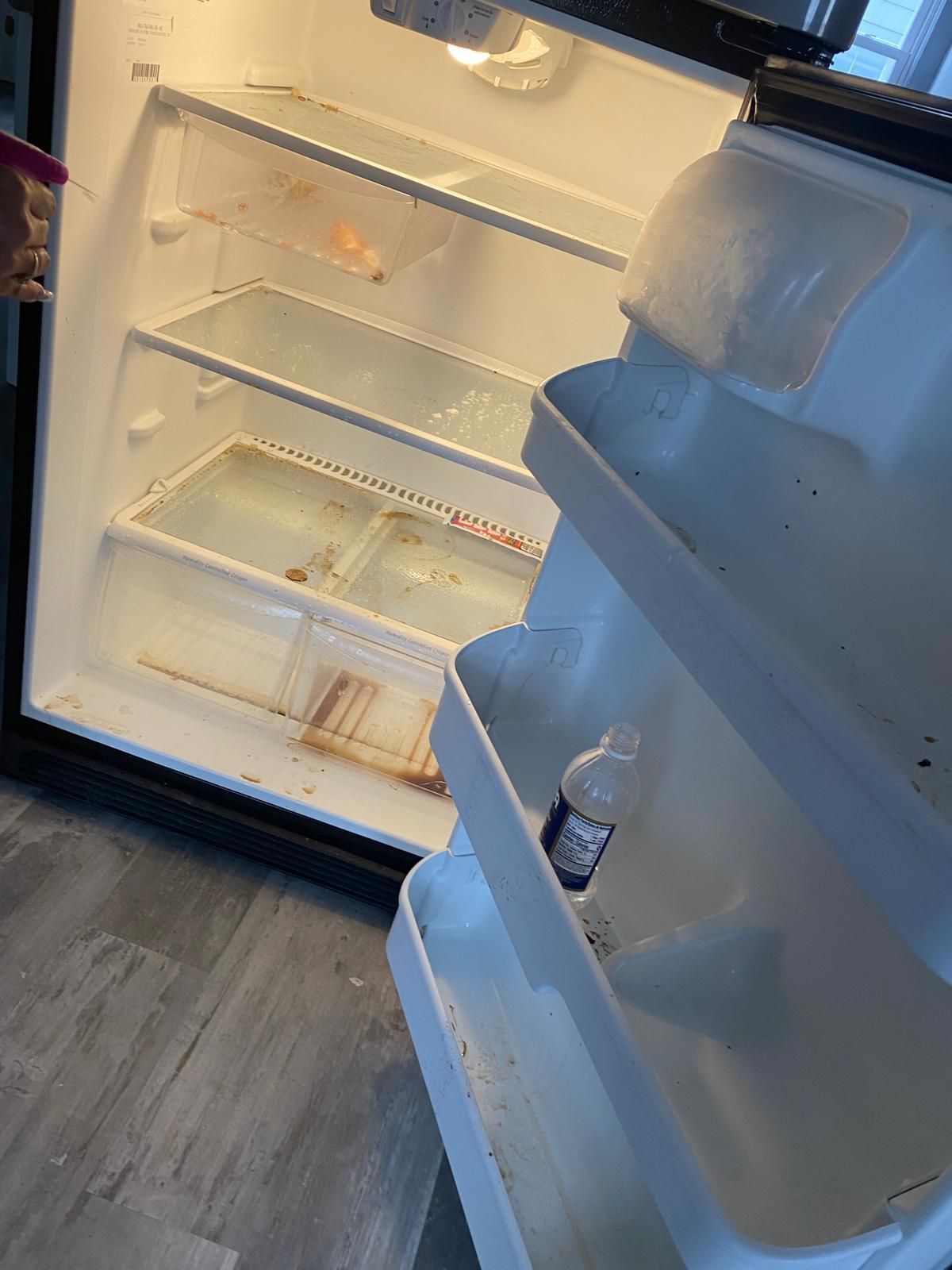 Open refrigerator interior with dirty shelves; a bottle rests in the door.