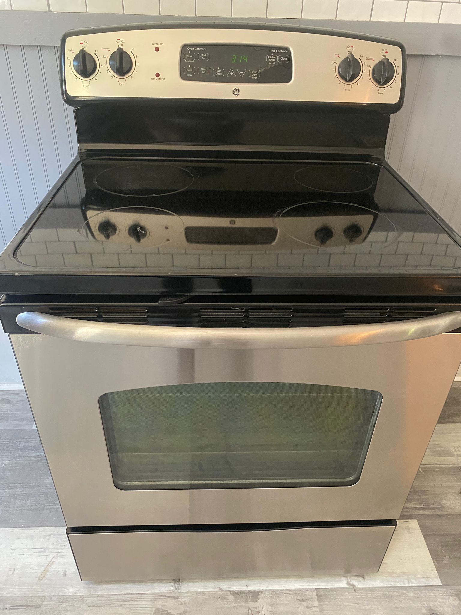 Stainless steel electric range with black cooktop and controls. Oven door open.