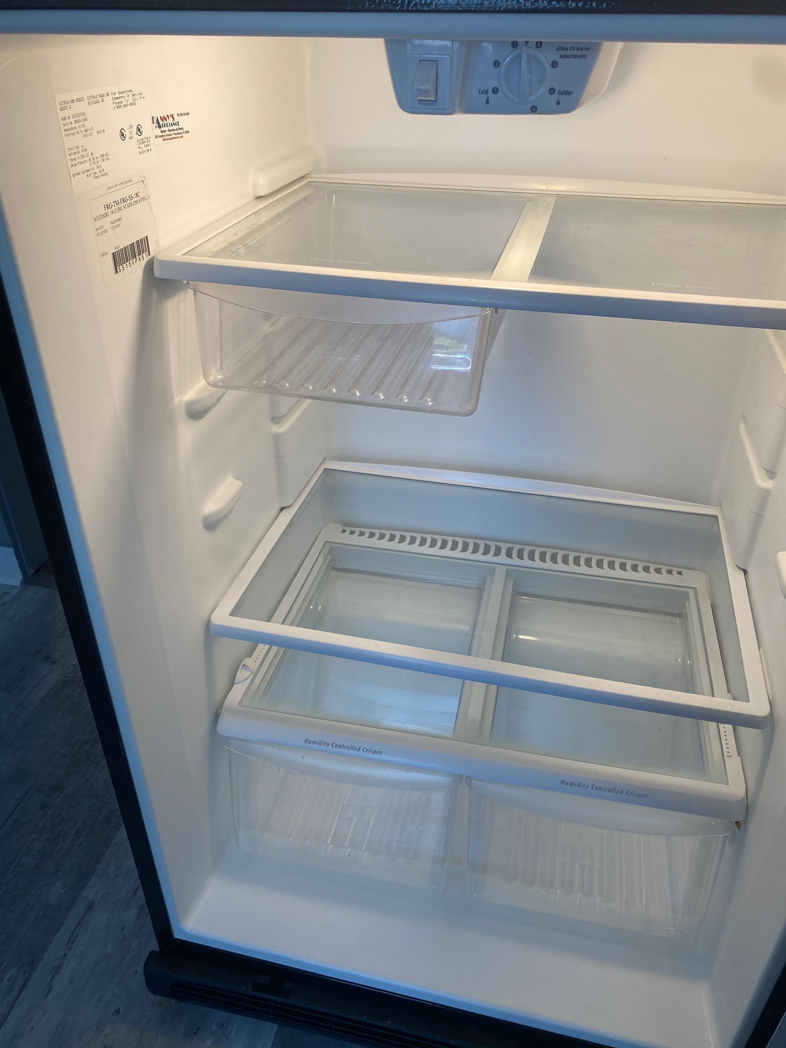 Empty refrigerator interior, white shelves and drawers, overhead lighting.