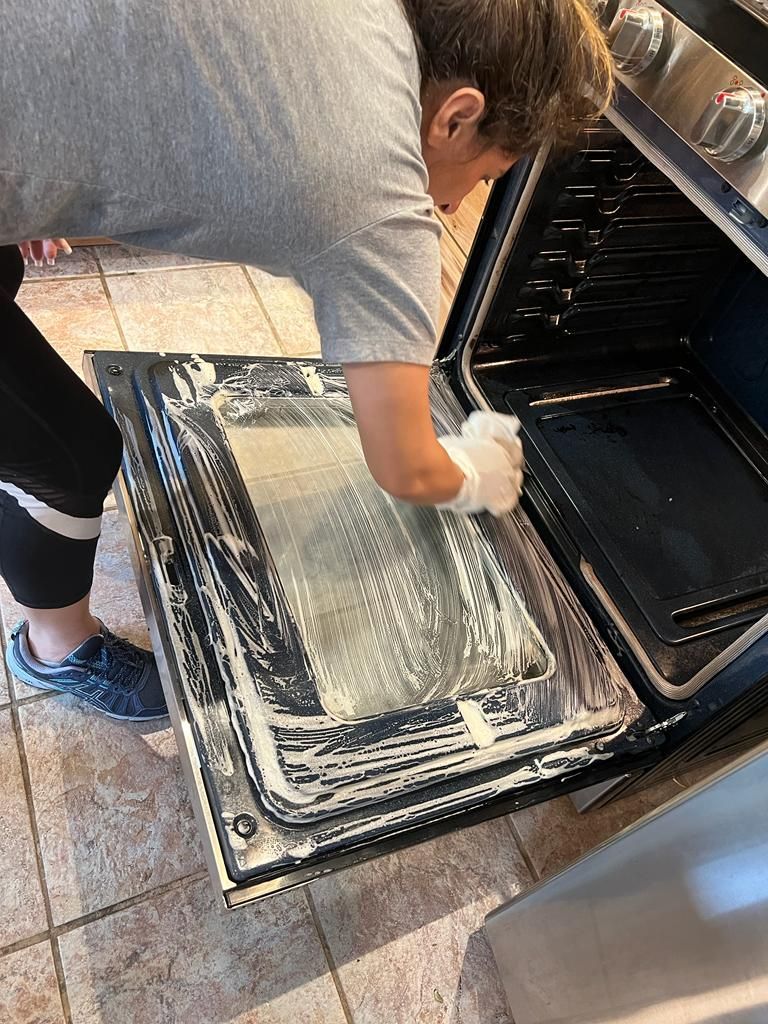 Person wearing gloves cleaning an oven door with cleaning product.