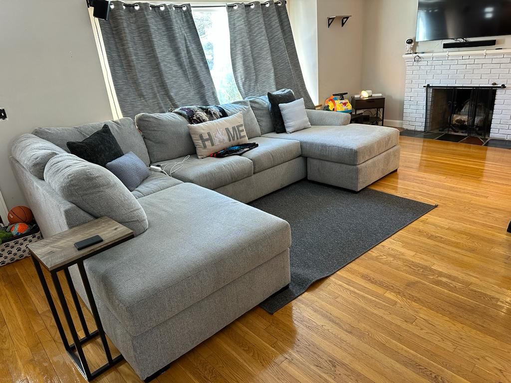 Grey sectional sofa in a living room with hardwood floors and a fireplace.