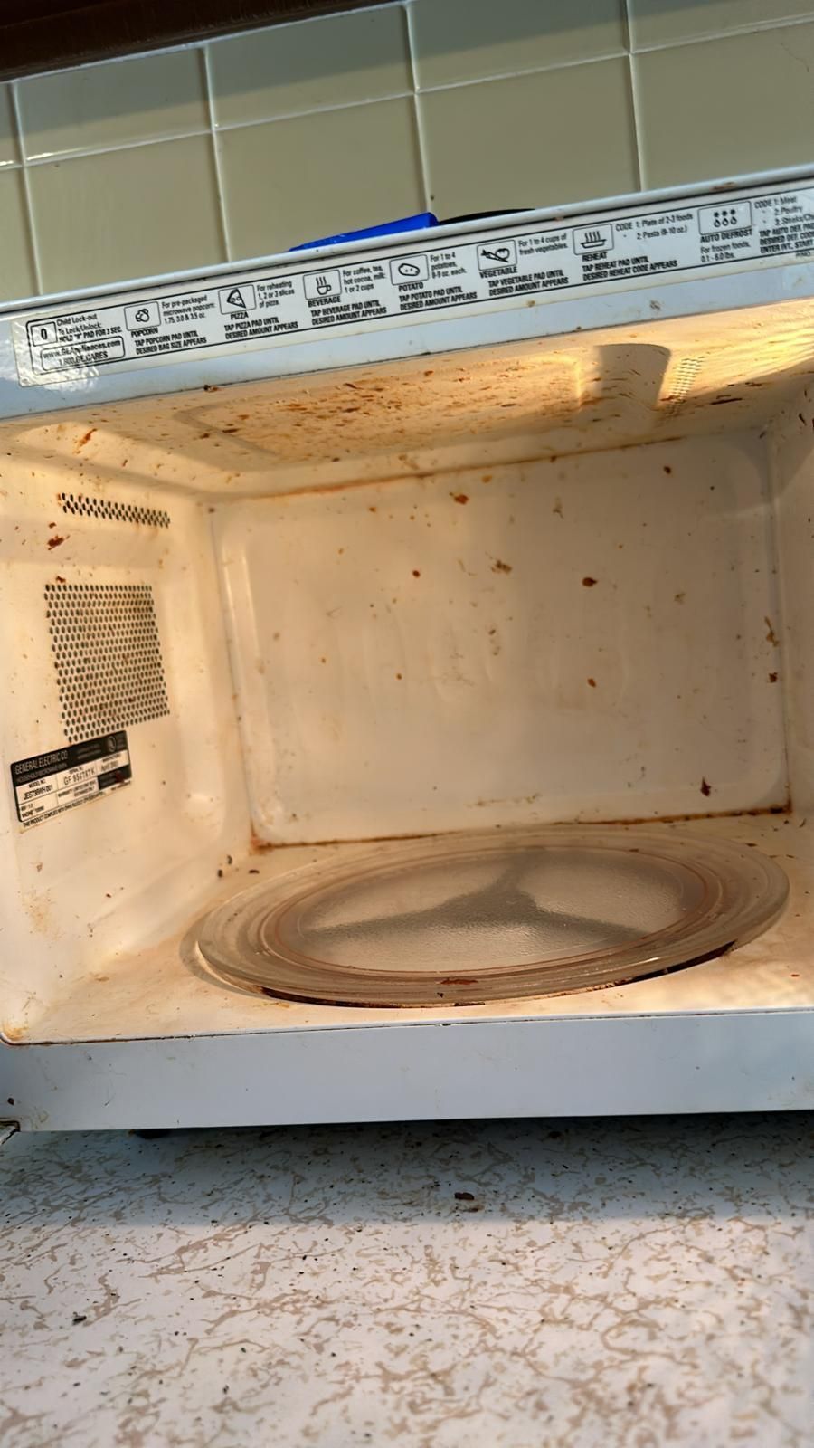 Dirty interior of a microwave with food splatters and a stained rotating plate.