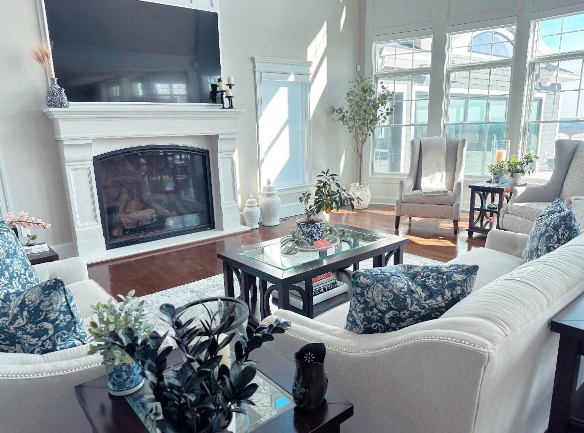 Living room with fireplace, white couches, large windows, and sunlight.
