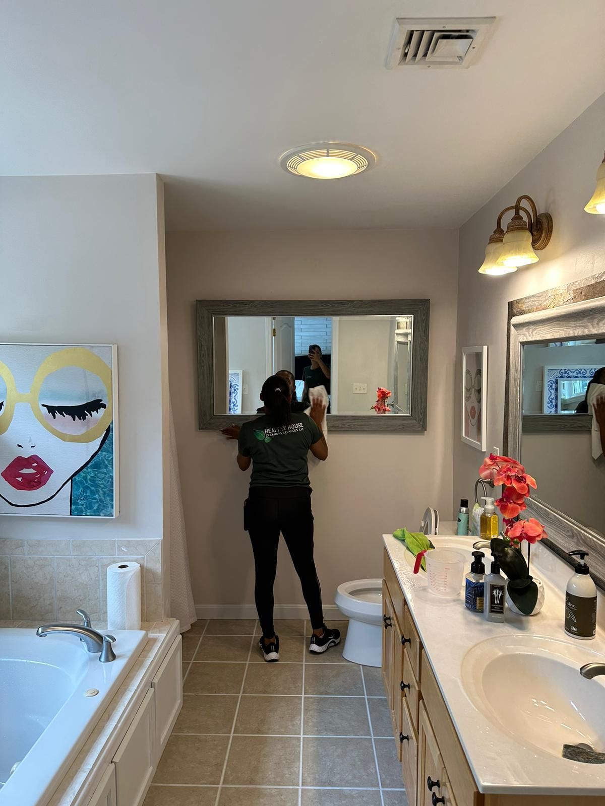 A person cleans a bathroom mirror in a well-lit bathroom with a jacuzzi and vanity.