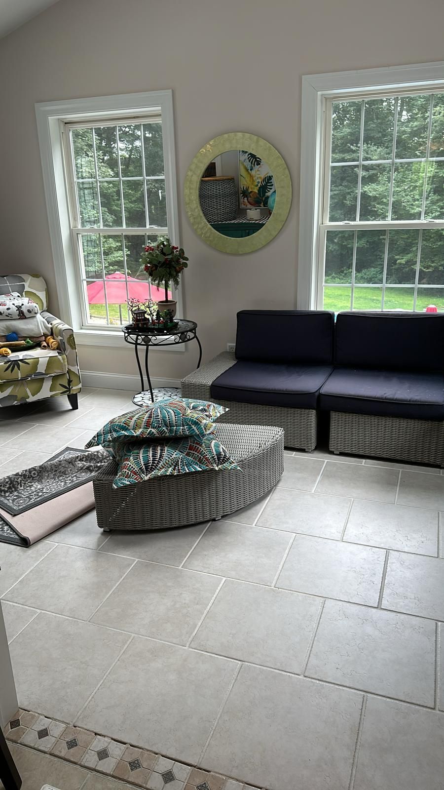 Sunroom with windows, stone floor, wicker sofa with blue cushions, and a decorative mirror.