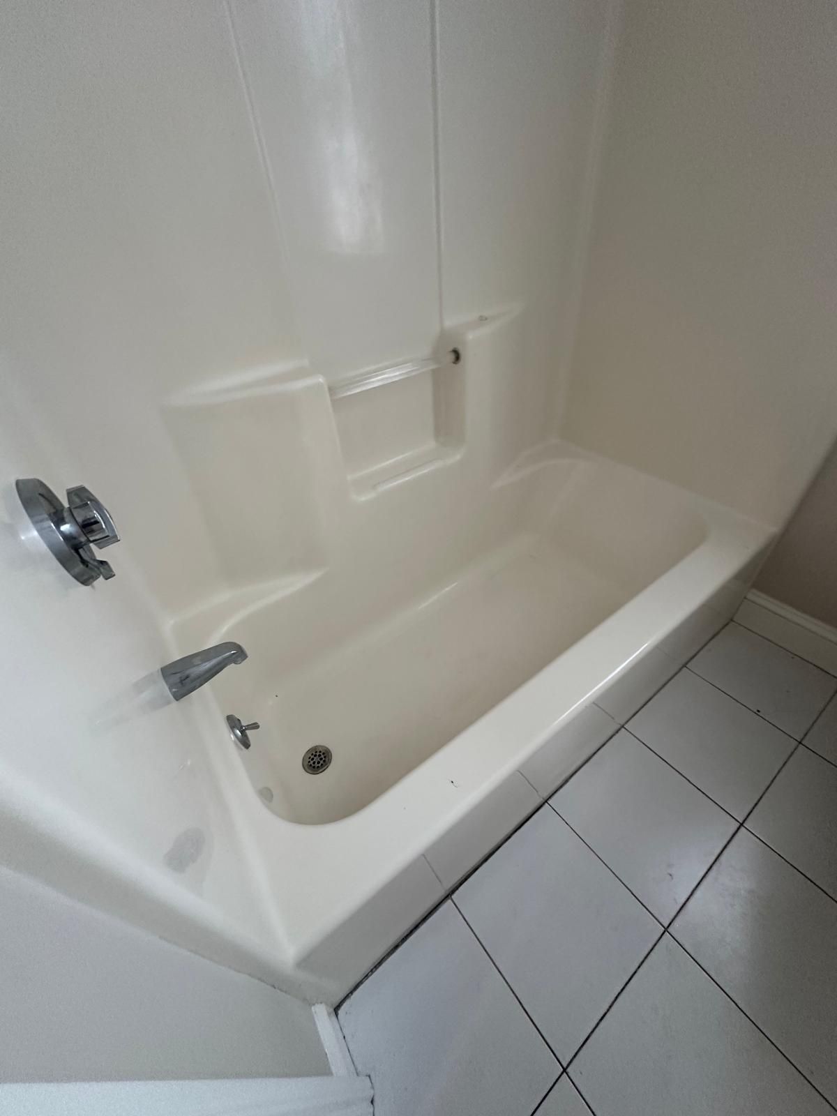 Beige bathtub with shower fixtures in a small bathroom with light tile flooring.