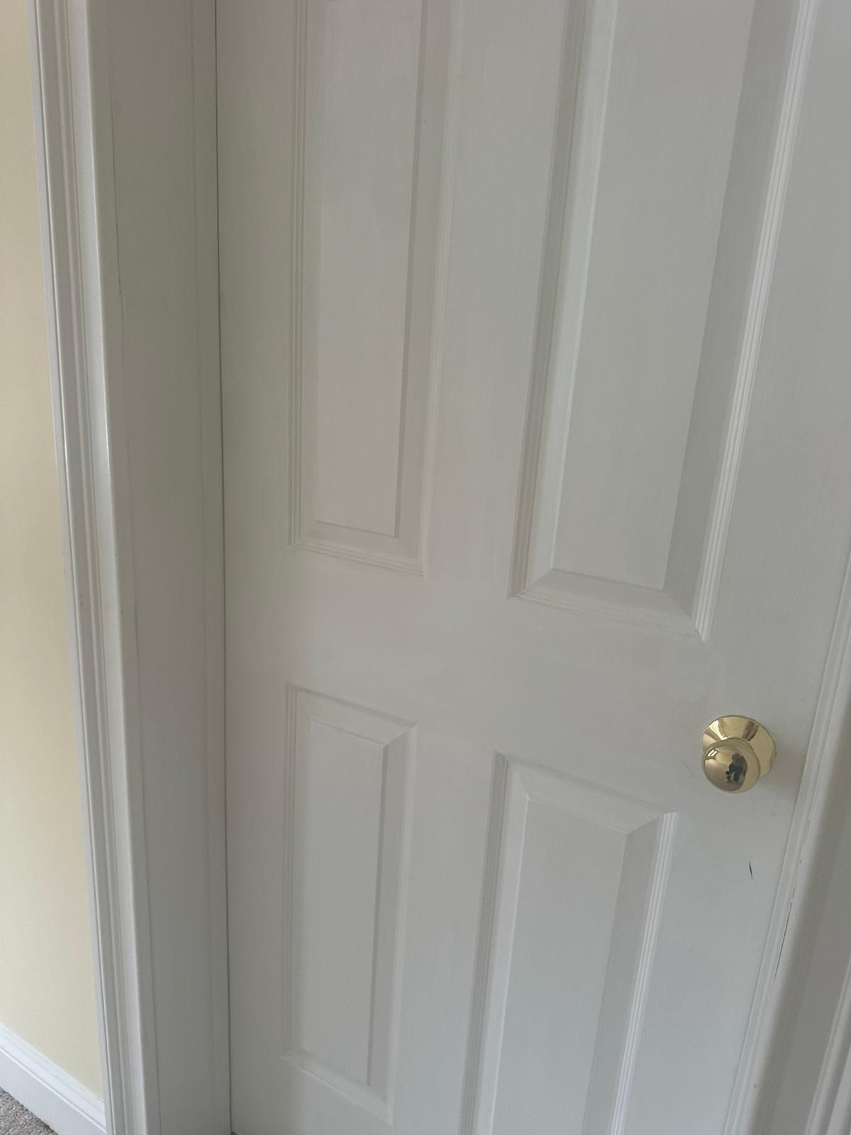 White, closed door with gold knob in a room; the door has four rectangular panels.