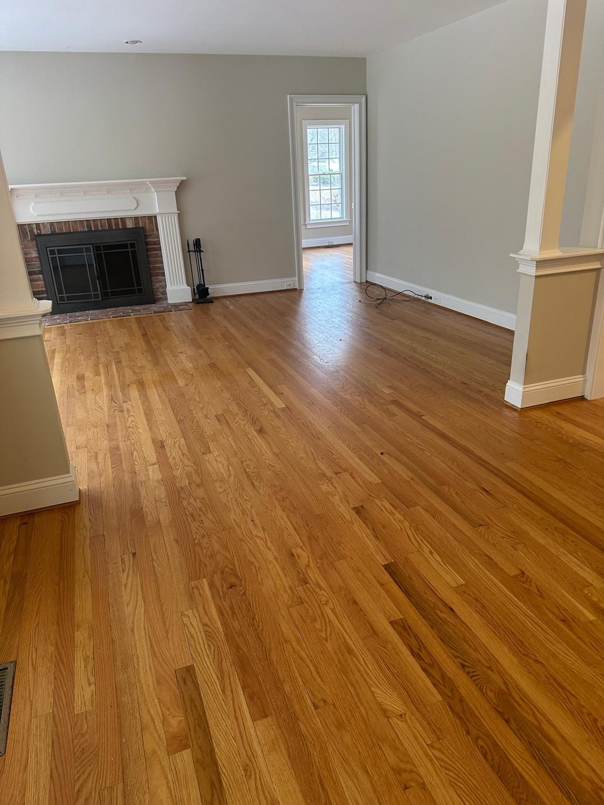 Hardwood floor in a living room with a fireplace, open doorway, and neutral-colored walls.