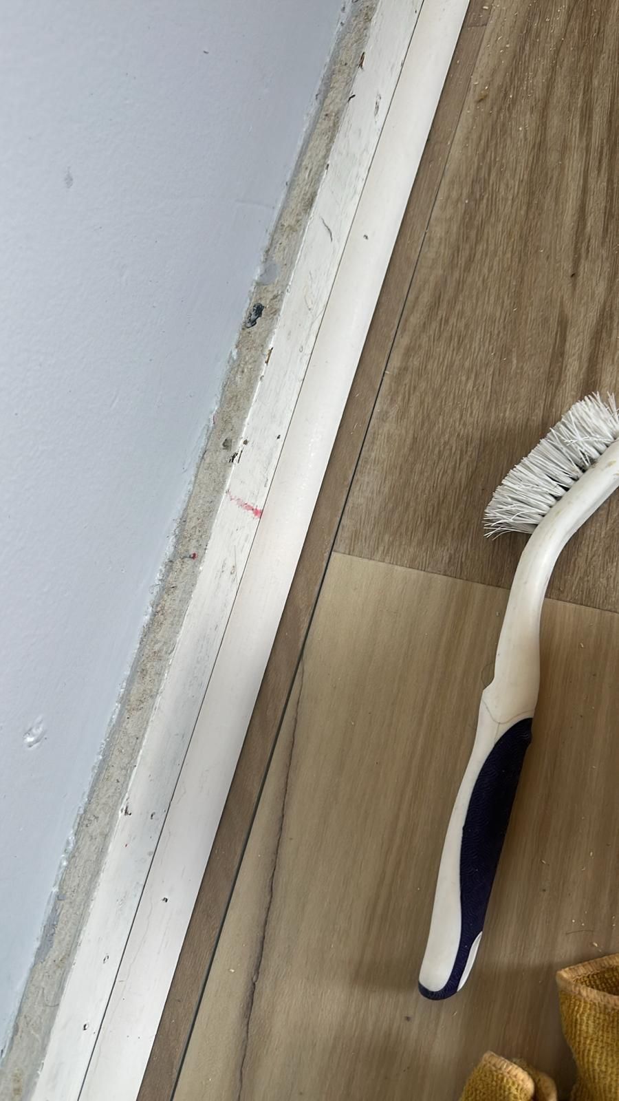 A white toothbrush near a white trim and brown floor.