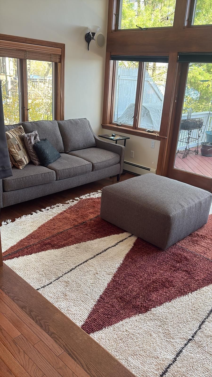 Living room with gray sofa, patterned rug, and large windows overlooking a deck.